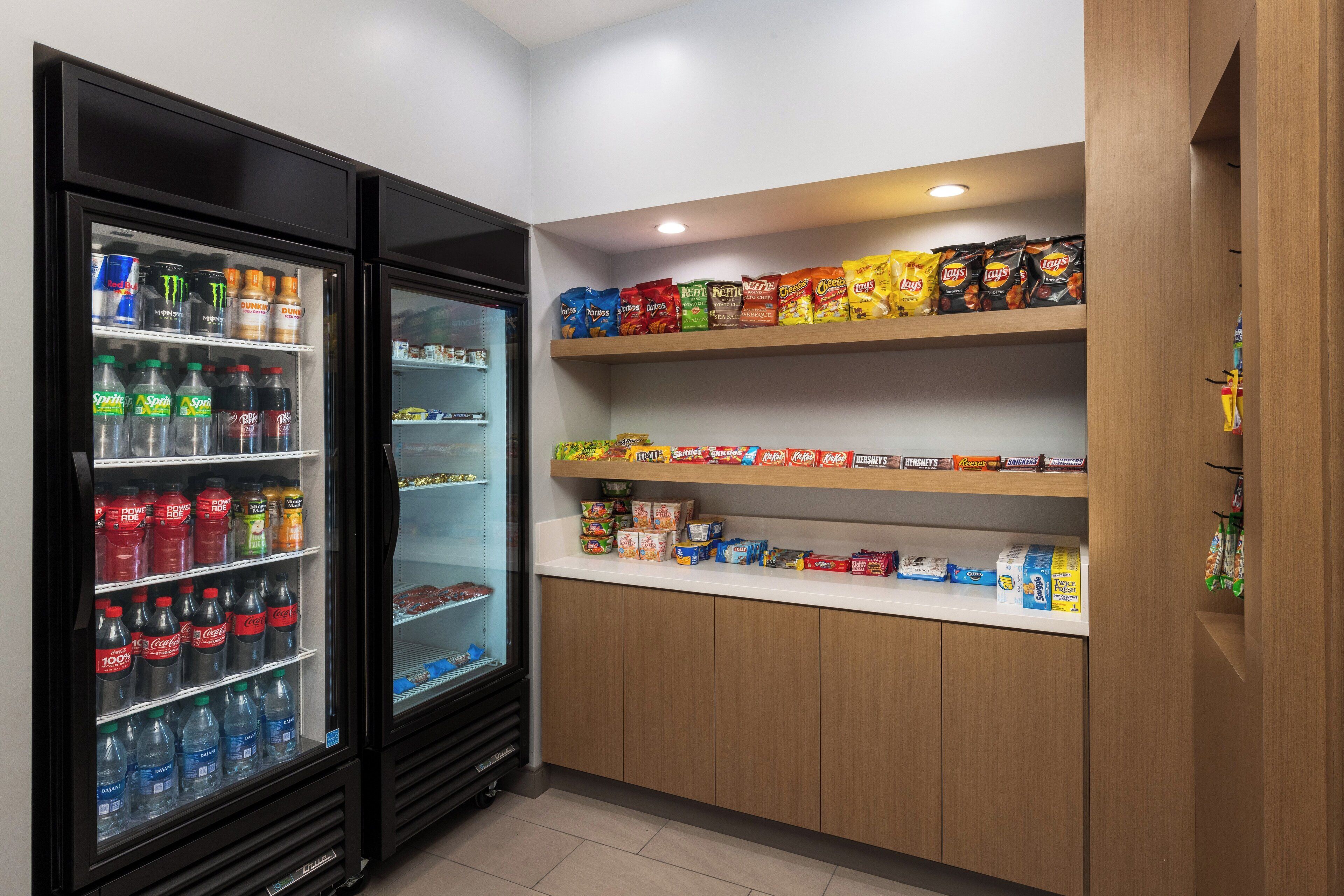 Un refrigerador con aperitivos y bebidas, repleto de refrescos y botanas como papas fritas, en una habitación limpia y bien iluminada.