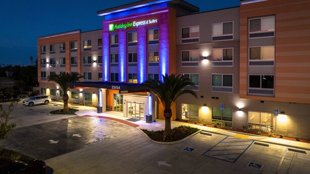 A Holiday Inn Express & Suites building with a modern design, featuring a prominent entrance, a parking lot, and a well-lit facade.