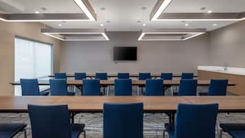 Un salón de conferencias con una larga mesa, sillas azules, un televisor de pantalla plana y una pequeña zona de kitchenette.