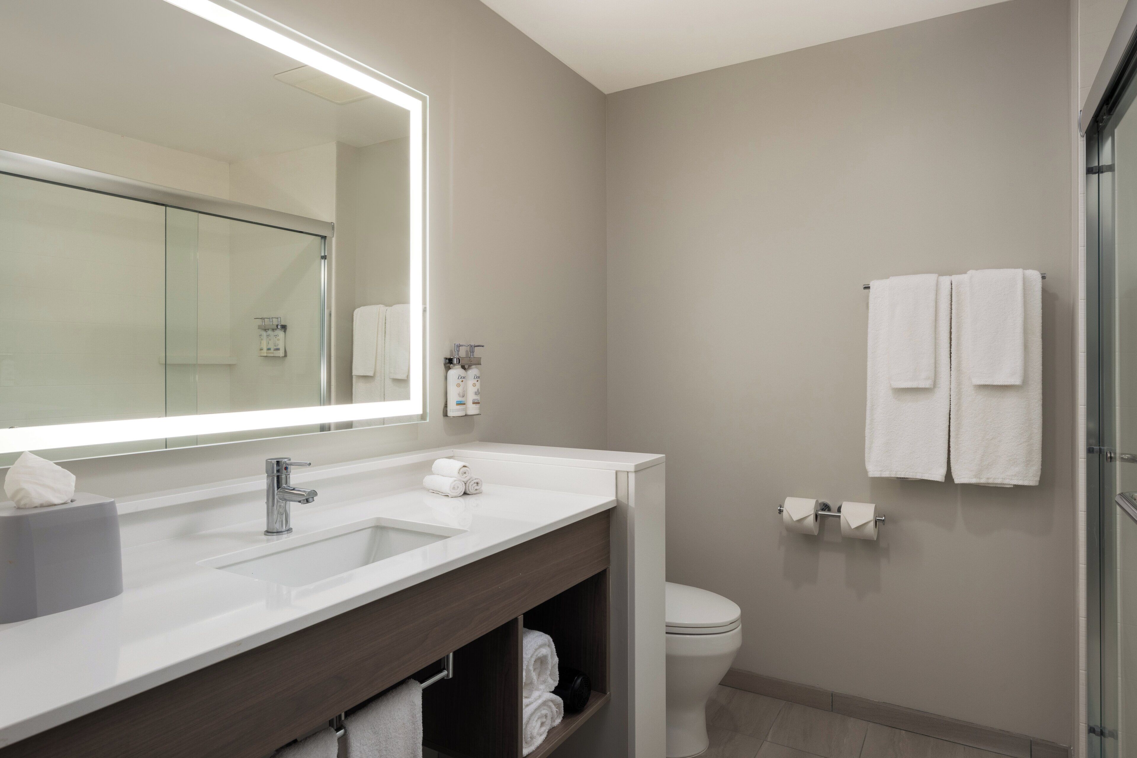 Un baño moderno con un espejo grande, lavamanos dobles, inodoro y cabina de ducha de vidrio.