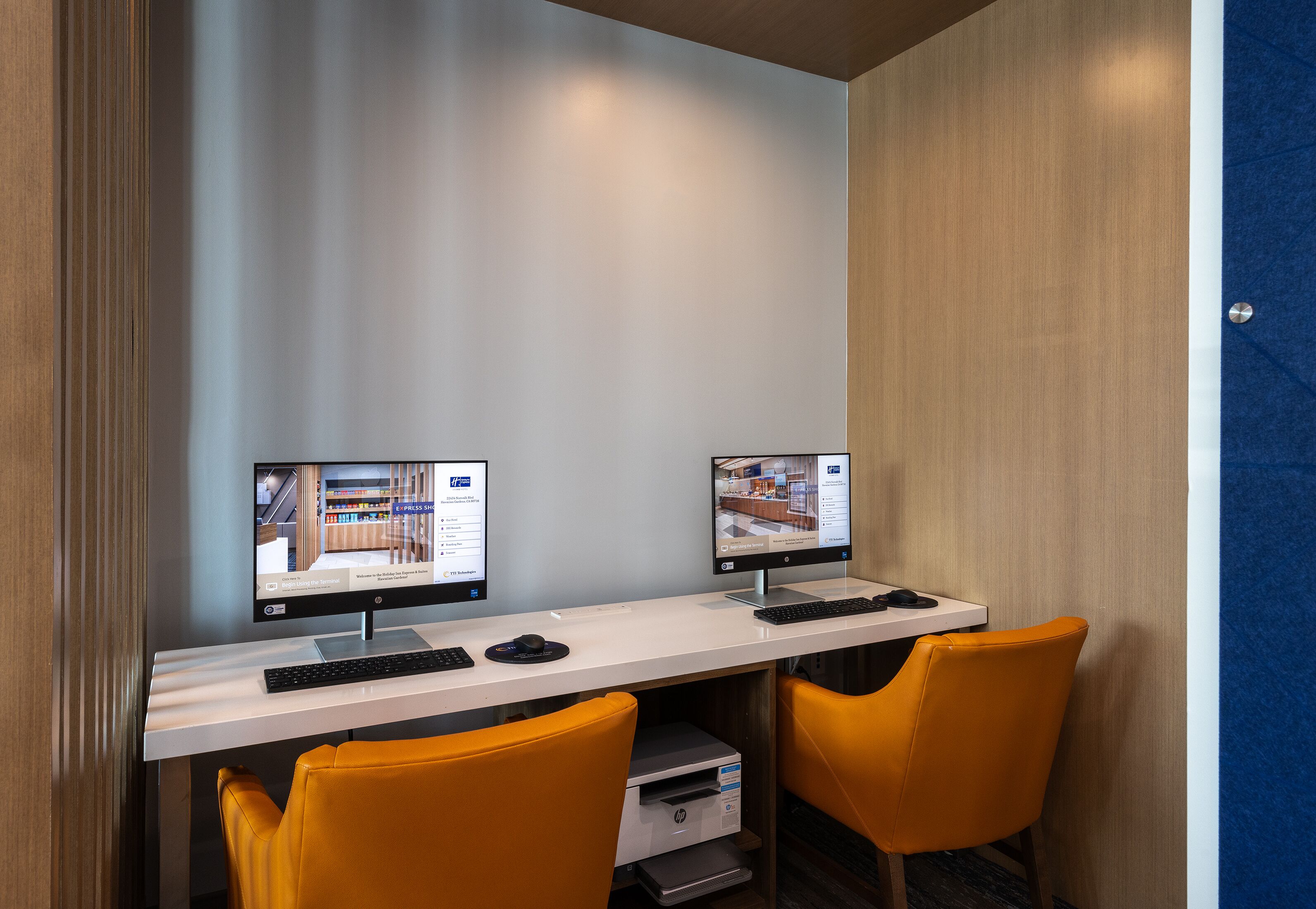 Een moderne kantoorruimte met twee computers op een bureau, een wit bureau en twee oranje stoelen.