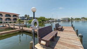 A wooden dock with benches and a lifebuoy, extending over calm water with boats in the background. - Floridian Flamingo Casita, 201 (Englewood)