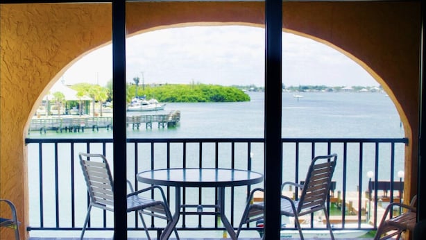 A balcony with a view of a body of water, a small island, and a dock with boats. There are two metal tables and four chairs. - Floridian Flamingo Casita, 201 (Englewood)