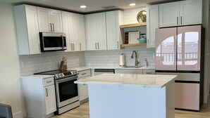 A modern kitchen with white cabinets, a central island, stainless steel appliances, and a view of the sea through a large window. - Floridian Flamingo Casita, 201 (Englewood)