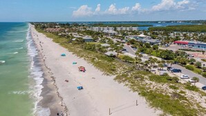 A beach with a row of beach umbrellas, a parking lot, and buildings in the background. - Floridian Flamingo Casita, 201 (Englewood)