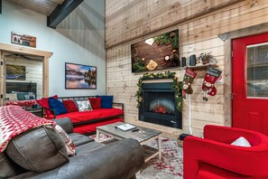 Une pièce chaleureuse avec une cheminée, un canapé rouge, un fauteuil en cuir marron et un mur en bois.