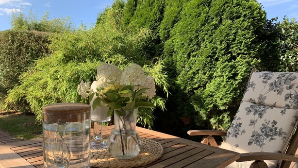 Une table en bois, un bocal en verre, un set de table en fibres tressées et un vase avec des fleurs blanches.