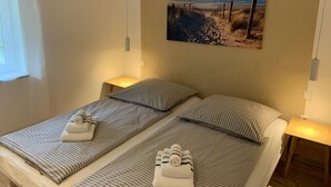 Une chambre avec deux lits, chacun agrémenté de draps et de serviettes à rayures, d’un tableau sur le thème de la plage au mur et de lampes de chevet.