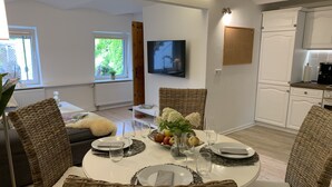 Un coin repas avec des chaises en osier, une table ronde dressée pour quatre personnes et un téléviseur fixé au mur.