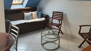 A cozy living room with a sofa, a wooden chair, a glass table, and a painting on the wall. - The Blue of 0pale (Cucq)