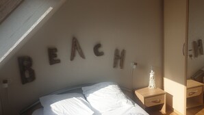 A bedroom with a bed, a nightstand, and a wall with wooden letters spelling "BEACH". - The Blue of 0pale (Cucq)