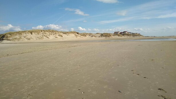 A wide sandy beach with footprints, dunes, and a building in the distance. - The Blue of 0pale (Cucq)