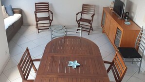 A dining area with a wooden table and chairs, a sofa, a television on a cabinet, and a framed picture on the wall. - The Blue of 0pale (Cucq)
