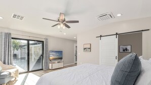 Et soveværelse med seng, ventilator, fjernsyn og en skydedør til en balkon.