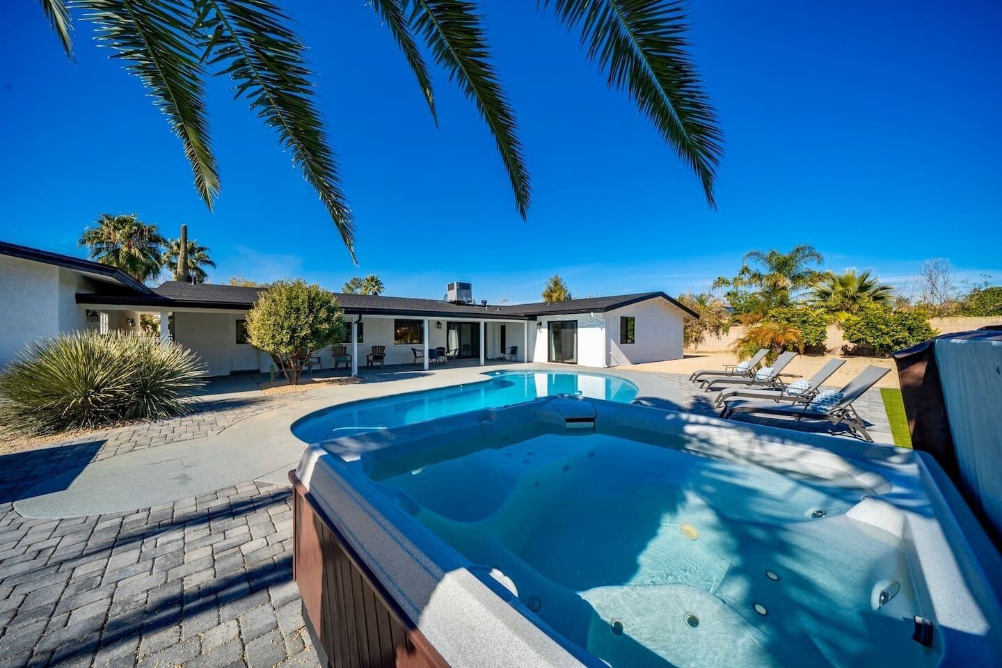 Ein modernes Haus mit Swimmingpool, Sitzgelegenheiten im Freien und Palmen.