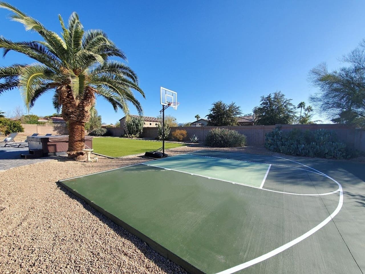Ein Basketballplatz im Freien mit einer Palme und blauem Himmel.