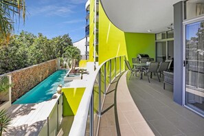 Un apartamento moderno con piscina, zona de comedor y balcón con barandilla de cristal.