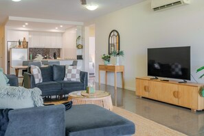 Uma sala de estar moderna com um sofá cinzento, uma mesa de centro e uma televisão sobre um móvel de madeira.