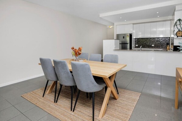 A modern kitchen with white cabinets, a stainless steel refrigerator, and a black backsplash.