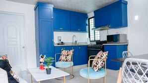 Una cocina moderna con armarios azules, encimera blanca y un comedor con mesa y sillas blancas.