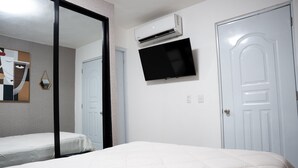 Un dormitorio con una cama, un televisor montado en la pared y un equipo de aire acondicionado.