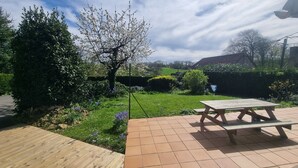 A garden with a wooden deck, a picnic table, and a grassy area with flowering plants.