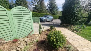 A driveway leading to a light blue car parked in front of a green gate.
