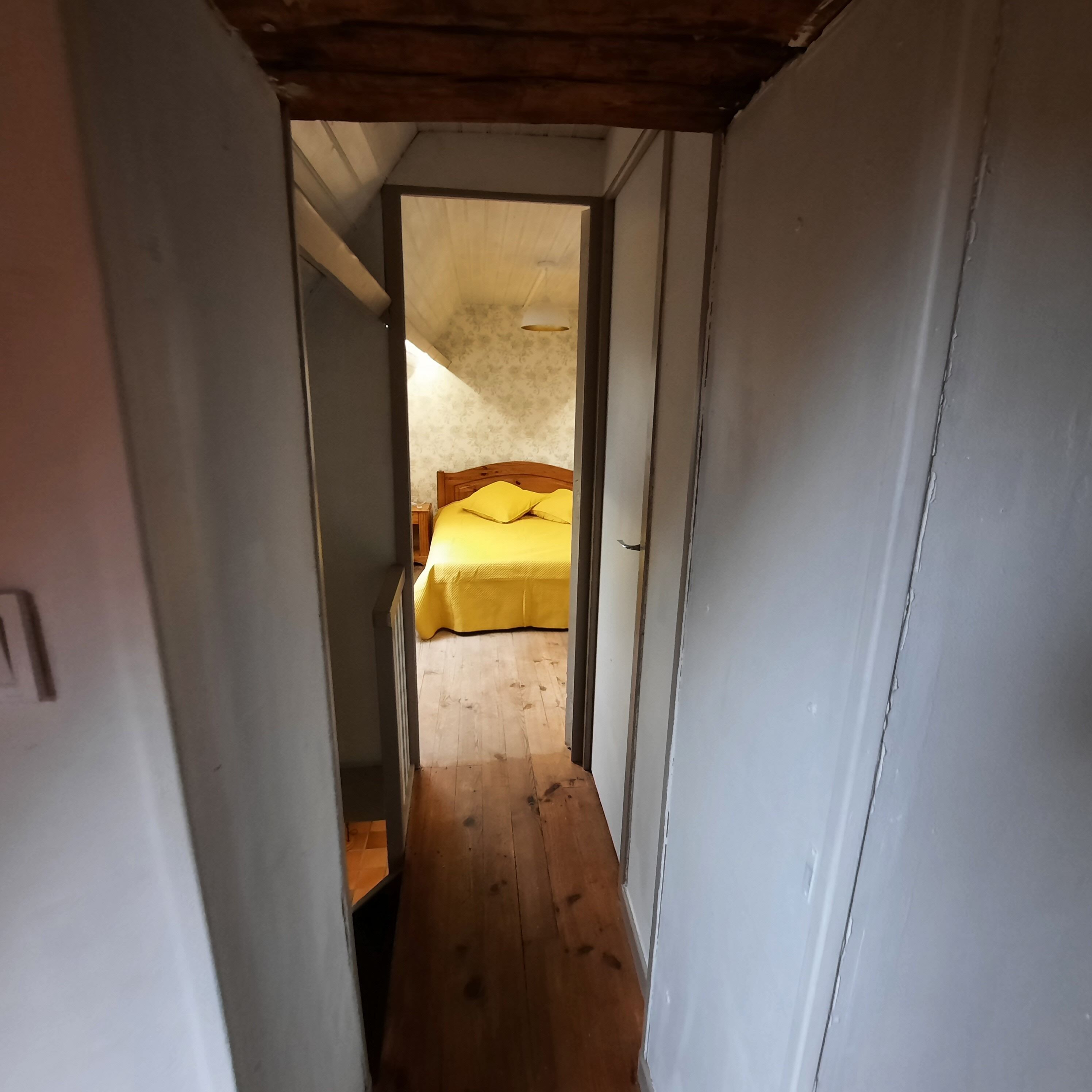 Un pasillo estrecho que conduce a un dormitorio con piso de madera y una cama con ropa de cama amarilla.