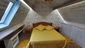 A small, cozy attic bedroom with a bed, a nightstand, a lamp, and a window.