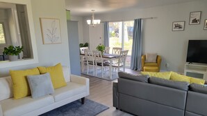 A modern living room with a white sofa, a grey sectional, and a yellow armchair. There is a dining area with white chairs and a table, and a TV on a white stand. - Bright, Modern Park Forest Home, 2.5m to Penn State! Breakfast included.  (State College)