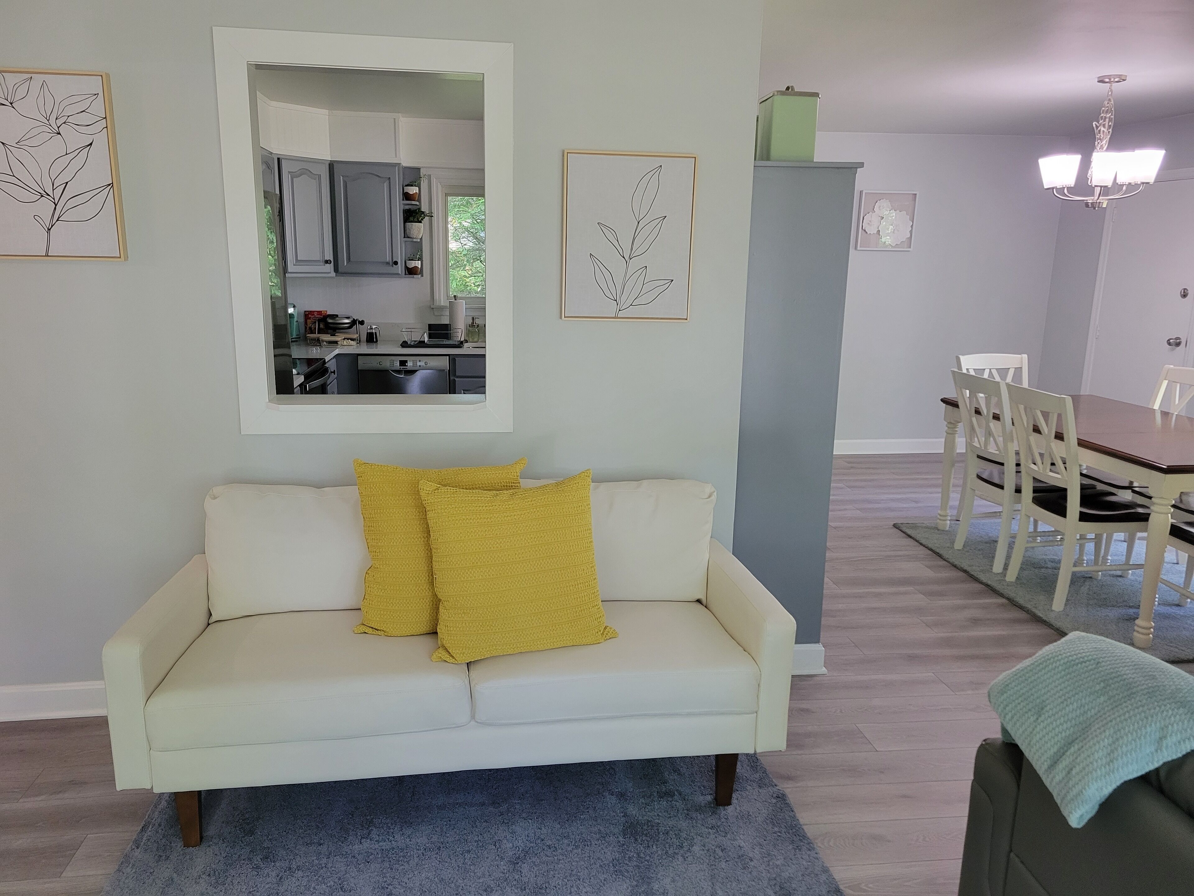 Un salon avec un canapé blanc, un tapis bleu et un coin repas comprenant une table et des chaises en bois.