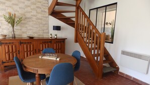 A dining area with a wooden table, blue chairs, a wooden staircase, and a brick floor. - Renovated 150-year-old building, close to Chateau de Menou. (Menou)