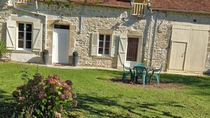 A stone building with a tiled roof, a grassy yard, and outdoor furniture. - Renovated 150-year-old building, close to Chateau de Menou. (Menou)