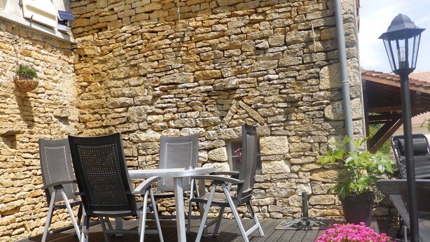 An outdoor seating area with a stone wall backdrop, metal chairs, a table, and a potted plant with pink flowers. - Renovated 150-year-old building, close to Chateau de Menou. (Menou)