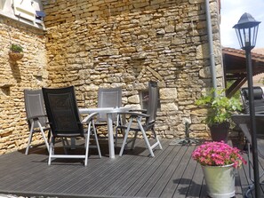 An outdoor seating area with a stone wall backdrop, metal chairs, a table, and a potted plant with pink flowers. - Renovated 150-year-old building, close to Chateau de Menou. (Menou)
