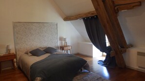 A bedroom with a sloped ceiling, a bed with a headboard, a bedside table with a lamp, and a window with curtains. - Renovated 150-year-old building, close to Chateau de Menou. (Menou)
