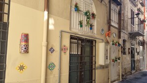 A narrow street with a building featuring a large metal gate, decorative tiles, and potted plants on the windowsills. - Typical Sicilian cottage equipped with all comforts at the centr (Palermo)