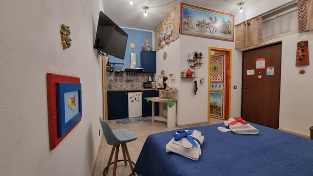 A compact room with a bed, a small kitchenette, a TV, and a door with a colorful mural. - Typical Sicilian cottage equipped with all comforts at the centr (Palermo)