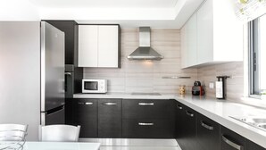 A modern kitchen with dark cabinetry, a stainless steel refrigerator, a microwave, and a gas stove. - Caminho da Praia - Pool & Beach Area (Peniche)