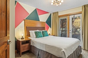 A hotel room with a large bed, wooden headboard, bedside tables with lamps, and a view through the window.