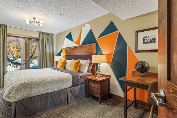 A hotel room with a bed, a desk, a lamp, a globe, and a framed photo on the wall.