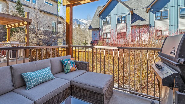 A covered outdoor seating area with a grill and a view of houses and mountains. - Family & Group Oasis: Hot Tub, AC, Fireplace, 2 Patios, Walk to Food & Shops (Canmore)