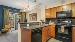 A kitchen with wooden cabinets, a black microwave, a stove, and a dishwasher. - Family & Group Oasis: Hot Tub, AC, Fireplace, 2 Patios, Walk to Food & Shops (Canmore)