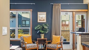 A cozy living room with a dark blue wall, a bookshelf, two patterned armchairs, a small table, and a potted plant. - Family & Group Oasis: Hot Tub, AC, Fireplace, 2 Patios, Walk to Food & Shops (Canmore)