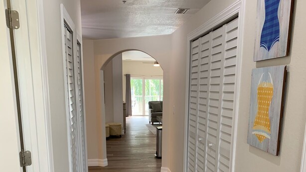 A hallway with wooden flooring, white walls, and a ceiling light. There are white doors and a window with curtains in the background. - Coastal Tranquility in Quiet, Gated Community (Rotonda West)