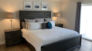 A modern bedroom with a dark wood headboard, a white textured bedspread, and two bedside tables with lamps. There are three framed artworks on the wall above the bed. - Coastal Tranquility in Quiet, Gated Community (Rotonda West)