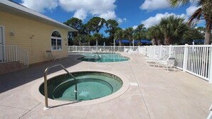 A pool area with two hot tubs, a white fence, and palm trees in the background. - Coastal Tranquility in Quiet, Gated Community (Rotonda West)