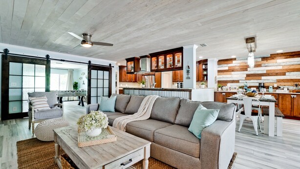 Amplia sala de estar con un sofá grande de color gris, barra de bar de madera y cocina con armarios de madera y salpicadero de piedra.