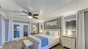 Un dormitorio con cama, mesita de noche, banqueta, ventilador de techo y ventana con persianas.