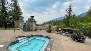Un bain à remous doté d’une structure en pierre, entouré d’une clôture et d’une piscine.